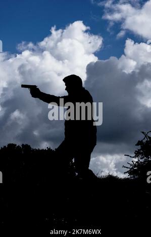 Silhouette d'homme avec un fusil contre un ciel nuageux style couverture de livre. Banque D'Images
