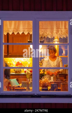 Une femme travaillant dans une cuisine vue par une fenêtre la nuit Banque D'Images