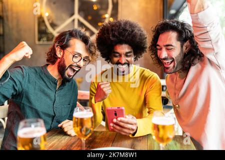 Trois amis multiraciaux excités célébrant le pari en ligne gagnant sur le match Banque D'Images