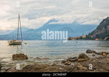 Lac de Côme avec la ville de Varenna, vue depuis le lac rocheux, un bateau à voile amarré en premier plan Banque D'Images