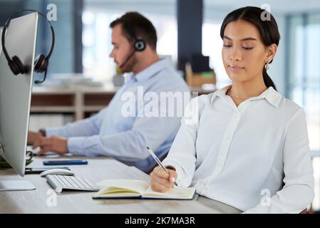 Je dois faire une note avant d'oublier. une jeune femme qui écrit dans un ordinateur portable tout en travaillant dans un centre d'appels moderne. Banque D'Images