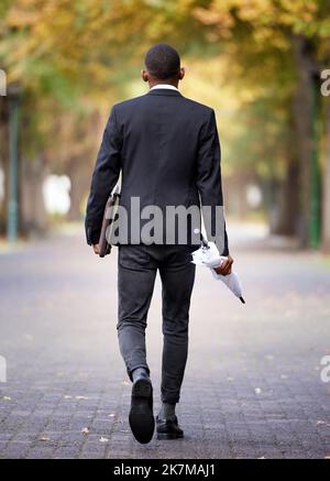 Prêt pour le travail. Vue arrière d'un homme d'affaires méconnu qui marche dans un parc de la ville. Banque D'Images