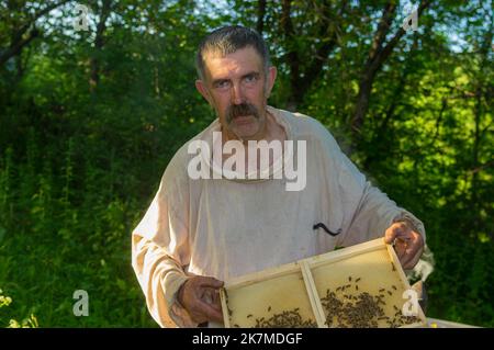 Beau portrait extérieur de paysan ukrainien prenant le cadre avec des abeilles tout en travaillant dur dans sa propre cour d'abeilles Banque D'Images