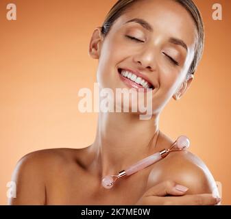 Femme beauté, massage du visage et rouleau de quartz rose, produit cosmétique de soin de la peau ou outil de maquillage brillant sur fond gris studio. Sourire, heureux et Banque D'Images