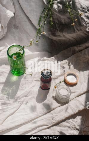 Développement durable concept cosmétique fond marron verre vert verre fleurs camomille voile avec produit plat couché vert naturel beauté concept de blog Banque D'Images