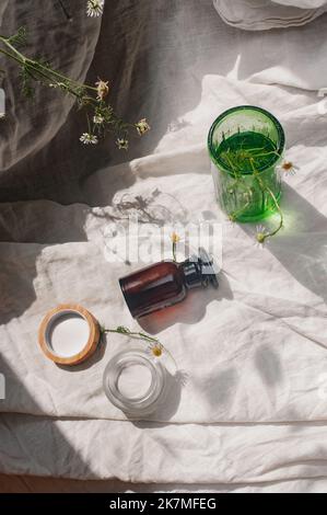 Développement durable concept cosmétique fond marron verre vert verre fleurs camomille voile avec produit plat couché vert naturel beauté concept de blog Banque D'Images