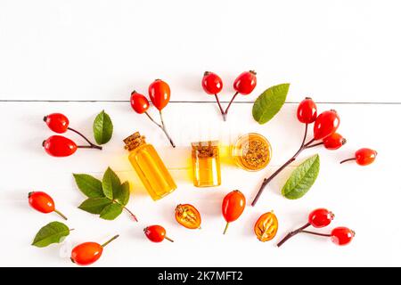 vue de dessus de plusieurs bouteilles différentes avec un liège à l'huile de rosehip naturelle. feuilles vertes et hanches roses. arrière-plan blanc. médecine alternative Banque D'Images