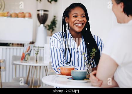 Bonne jeune femme d'affaires souriant tout en prenant un café avec un collègue dans un café. Deux femmes d'affaires gaies ayant une conversation amicale Banque D'Images