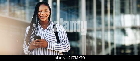 Une jeune femme d'affaires heureuse souriant à la caméra tout en se rendant au travail en ville. Portrait d'une jeune femme d'affaires gaie utilisant un smartphone Banque D'Images