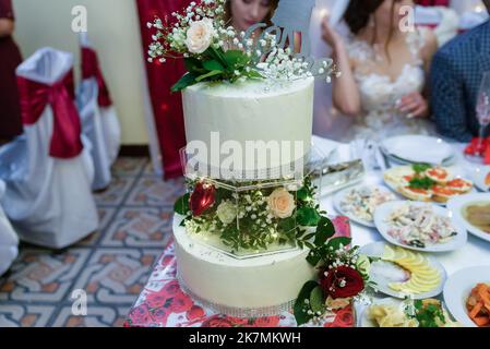 Gâteau de mariage blanc décoré de fleurs sur une table de fête avec beaucoup d'en-cas sur le côté. Fleurs violettes au premier plan. Mariage. Réc Banque D'Images