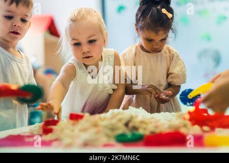 donnez-moi cette figure rouge - les enfants jouant avec le sable cinétique, plan moyen flou de fond de la maternelle concept. Photo de haute qualité Banque D'Images