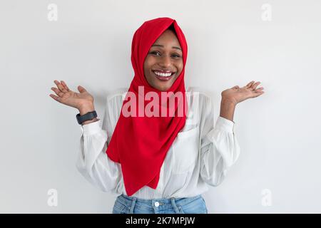 Qui s'en soucie. Femme musulmane afro-américaine insouciante dans le hijab se propageant les mains et haussant les épaules, mur blanc Banque D'Images
