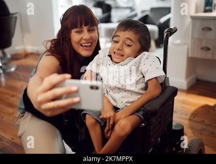 Enfant, paralysie cérébrale et téléphone heureux selfie d'un garçon handicapé mobile dans un fauteuil roulant. Une femme ou une mère sourit avec un jeune enfant en utilisant la technologie pour Banque D'Images