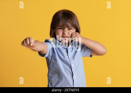 Colère et émotions des enfants. Furieux petit garçon montrant des poings à la caméra, se sentant ennuyé, orange studio arrière-plan Banque D'Images