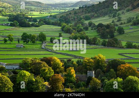 Paysage pittoresque de Dales (couleur d'automne sur les arbres, vaste fond plat de la vallée, pentes abruptes à flanc de colline, vieilles granges en pierre) - Kettlewell, Yorkshire Angleterre Royaume-Uni. Banque D'Images