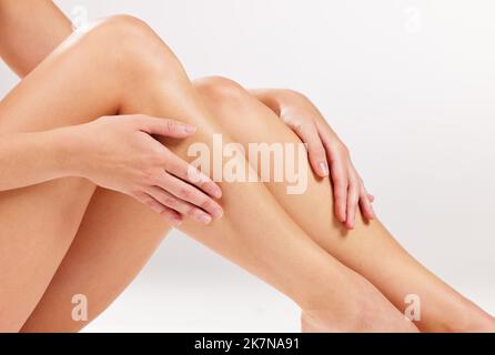 Un toucher impeccable. Photo studio d'une jeune femme méconnue qui touche ses jambes tout en posant sur un fond gris. Banque D'Images