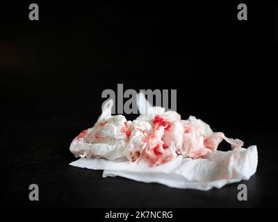 Sang rouge frais taché sur du papier de soie isolé sur fond sombre, utilisé papier essuie-tout froissé, fond perdu, espace de copie Banque D'Images