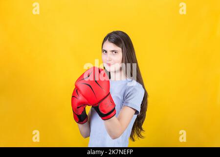 Une jeune femme confiante avec des gants de boxe rouges se tient en position de combat. Portrait d'une fille forte et déterminée préparée pour la bataille isolée sur yello Banque D'Images