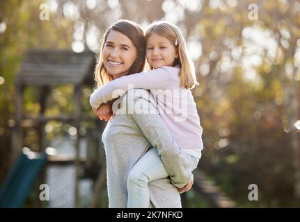 Elle adore les promenades en porcgyback. Portrait court d'une jeune femme attrayante et de sa fille posant à l'extérieur dans le jardin à la maison. Banque D'Images