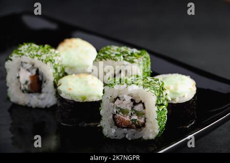 Ensemble de petits pains à sushis sur une assiette noire. Rouleaux uramaki et futomaki avec sauce wasabi. Il sert de la cuisine japonaise au restaurant. Plat asiatique populaire de riz et s. Banque D'Images