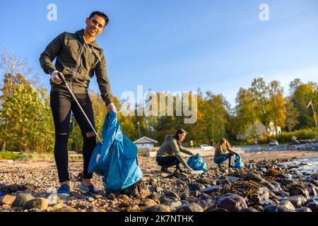 Homme nettoyant la plage avec un groupe de bénévoles le jour ensoleillé Banque D'Images