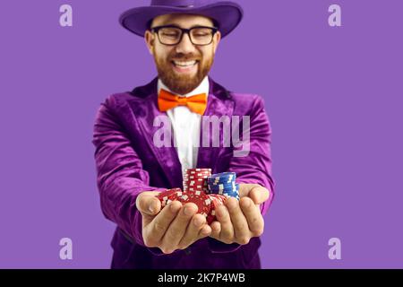 Gros plan des jetons de poker entre les mains d'un homme joyeux et satisfait isolé sur fond violet. Banque D'Images
