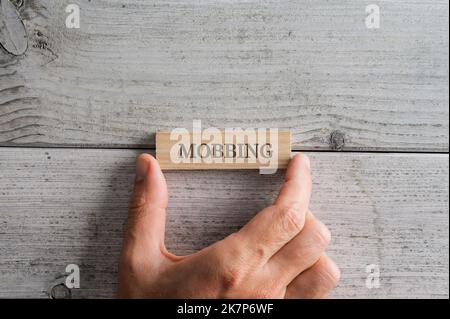 Main mâle plaçant une cheville en bois avec signe Mobbing sur elle sur fond blanc texturé en bois. Banque D'Images