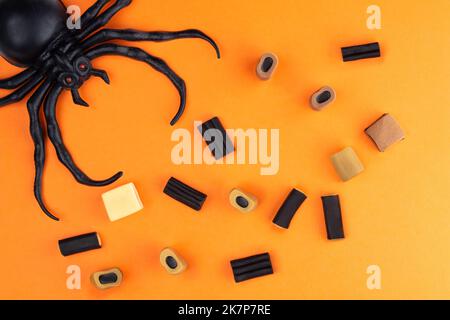 Composition à Halloween de divers bonbons et araignées dans le coin du cadre, sur fond orange. Banque D'Images