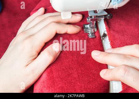 couturière les mains cousues sur la fermeture à glissière sur l'article rouge de vêtements par machine à coudre moderne avec le pied de presse spécial. processus de couture Banque D'Images
