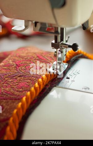 Équipement professionnel. Machine à coudre moderne avec pied de pression spécial. Le processus de couture d'une corde décorative de bordure de l'article rouge de vêtements. Banque D'Images