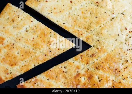 Pizza en tranches sur fond de pierre noire, vue du dessus. Focaccia fraîchement cuit avec du fromage Banque D'Images