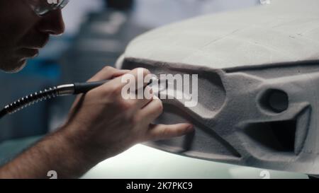 Le concepteur et développeur de voitures senior utilise un outil rotatif de type stylo pour affiner la sculpture de râteau d'un prototype de voiture dans un studio de haute technologie. Effectue les corrections de conception. Industrie automobile. Banque D'Images