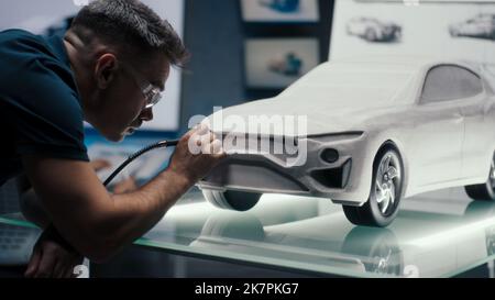 L'ingénieur automobile apporte les corrections de conception à une sculpture de voiture prototype et la perfectionne à l'aide de la machine à outils rotative. Modèle de la voiture placé sur une table en verre dans un laboratoire de haute technologie. Banque D'Images