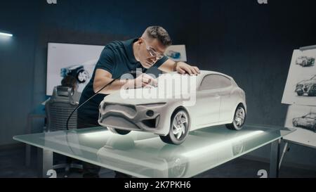 L'ingénieur automobile apporte les corrections de conception à une sculpture de voiture prototype. Le perfectionner à l'aide de la fraiseuse. Un laboratoire de haute technologie avec LED et croquis d'un nouveau modèle de voiture. Banque D'Images