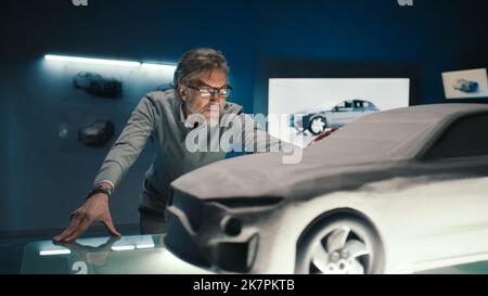 L'ingénieur automobile touche le modèle de la voiture prototype faite d'argile pour apporter des changements finaux dans la conception. Développeur de voitures à cheveux gris avec verres encadrés dans une entreprise de fabrication de voitures. Banque D'Images