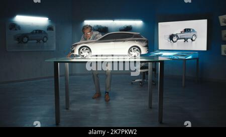 L'ingénieur automobile touche le modèle de la voiture prototype faite d'argile pour apporter des changements finaux dans la conception. Développeur de voitures à cheveux gris avec verres encadrés dans une entreprise de fabrication de voitures. Banque D'Images