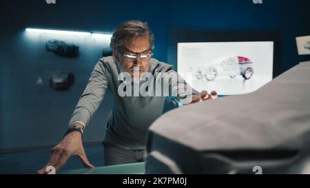 L'ingénieur automobile touche le modèle de la voiture prototype faite d'argile pour apporter des changements finaux dans la conception. Développeur de voitures à cheveux gris avec verres encadrés dans une entreprise de fabrication de voitures. Banque D'Images