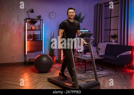 Portrait de jeune sportif actif beau asiatique sportif en noir entraînement de sport à la maison, marche, exercice cardio, sur tapis roulant à l'heure du soir. Concept de sport, soins de santé. Banque D'Images