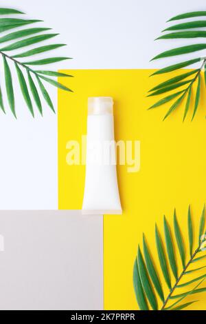 Tube blanc de crème cosmétique avec paume sur jaune. Pose à plat. Banque D'Images
