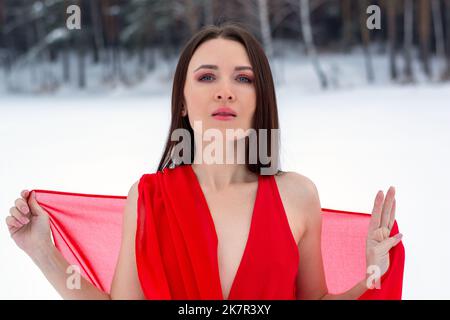 belle fille brune dans une robe rouge mince et pieds nus dans la forêt d'hiver. Banque D'Images