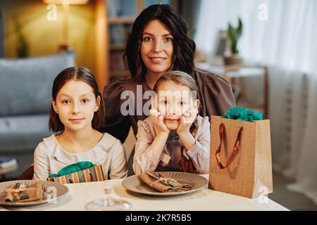 Portrait d'une mère juive moderne avec deux enfants regardant l'appareil photo tout en étant assis à la table du dîner dans un cadre confortable Banque D'Images