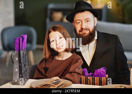 Portrait de l'homme juif moderne avec sa fille regardant l'appareil photo tout en étant assis à la table du dîner dans un cadre confortable Banque D'Images