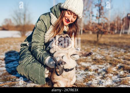 Jeune femme marchant chien de pug dans un parc d'hiver enneigé jouant avec un animal de compagnie tenant un animal sur les pattes arrière.Activités de plein air en saison Banque D'Images