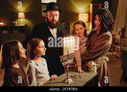 Portrait de famille juive moderne regardant la bougie de menorah d'argent pendant la célébration de Hanoukkah dans une maison confortable Banque D'Images