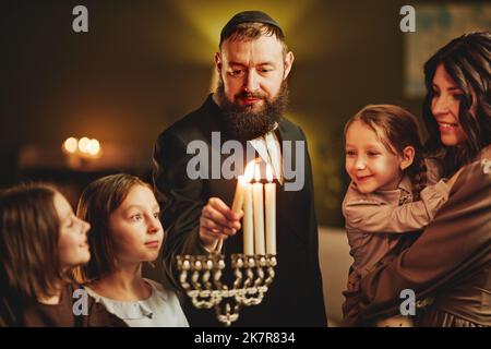 Portrait de l'homme juif orthodoxe éclairant la bougie menorah avec la famille pendant la célébration Hanoukkah Banque D'Images