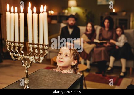 Portrait d'une petite fille juive regardant la bougie de menorah en admiration tout en célébrant Hanoukkah avec la famille, l'espace de copie Banque D'Images