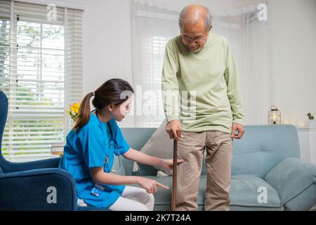 Médecin asiatique demandant et explication homme âgé au sujet des symptômes de douleur avec bâton de marche, jeune femme infirmière vérifiant le genou et la jambe après la chirurgie de l'aîné Banque D'Images