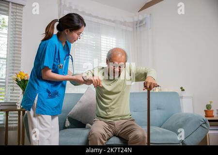 Infirmière soignante aidant à soutenir un homme handicapé senior pour se lever avec un bâton de marche, la jeune femme aide à soutenir les patients orthopédiques pour se lever avec le valin Banque D'Images