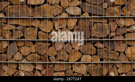 Mur de soutènement de gabion - gros plan de pierres brunes dans des paniers métalliques de gabion maintenus par un mur de soutènement. Banque D'Images