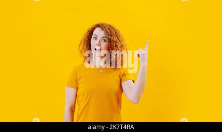 Apocalypse face d'une jeune femme avec des cheveux bouclés au gingembre pointant vers le haut. Sur fond jaune. Porter une chemise orange. Banque D'Images